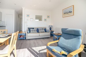 A living room with a sofa, a blue armchair, a dining table with chairs, and a kitchen area in the background. - 1 Bed in Gower (oc-hh9306) (Bishopston)