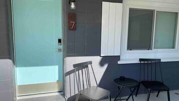 A teal door with a number '7' sign, two chairs, a small table, and a window with blinds.