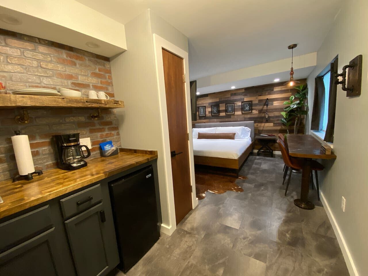 A compact hotel room with a kitchenette, a bed, a dining area, and a bathroom.