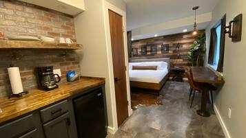 A compact hotel room with a kitchenette, a bed, a dining area, and a bathroom.