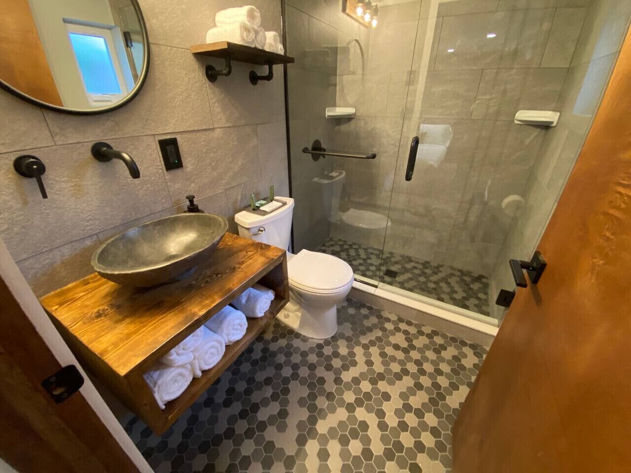 A bathroom with a wooden vanity, a large bowl sink, a toilet, and a glass shower enclosure.