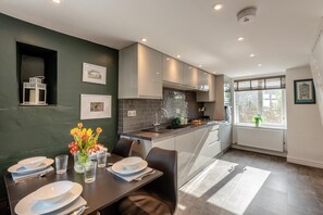 A modern kitchen with dark green walls, white cabinets, and a dining area with a table set for four. - 2 Bed in Dean (oc-h32066) (Dean)