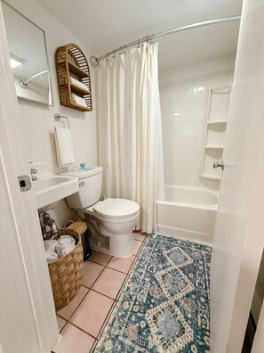 A bathroom with a toilet, sink, and bathtub. There is a shower curtain, a mirror, and a small shelf with towels. - Coastal Escape #5 Walk To Strip (Geneva)
