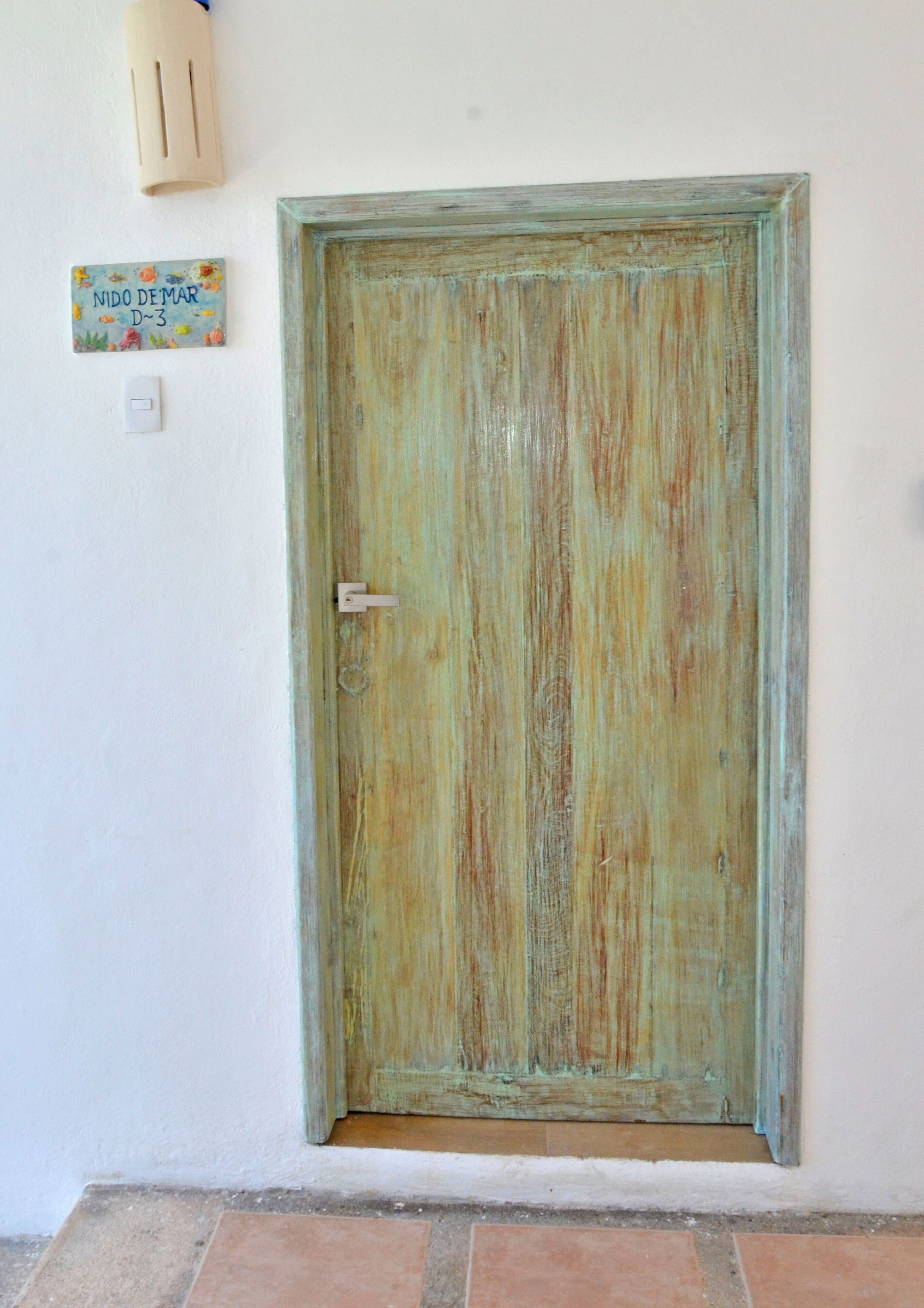 A rustic wooden door with a simple latch, a light switch, and a small sign above it.