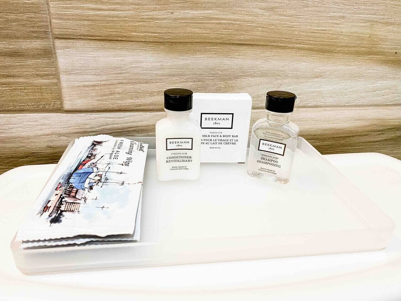 Un ensemble de produits de toilette disposés sur un plateau, comprenant un flacon de shampoing, un après-shampoing et un savon, avec un magazine à côté.