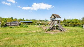 Een houten speelconstructie met een glijbaan en klimgedeelte in een grasveld.