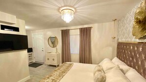 A hotel room with a large bed, a dresser, a vanity with a mirror, and a chandelier. - King Glamour #8, Walk to the Strip, A/C, WiFi (Geneva)
