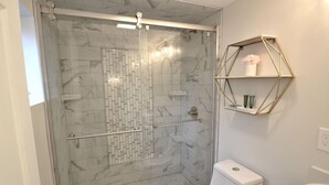 A bathroom with a glass-enclosed shower, a white toilet, and a geometric shelf with toiletries. - King Glamour #8, Walk to the Strip, A/C, WiFi (Geneva)
