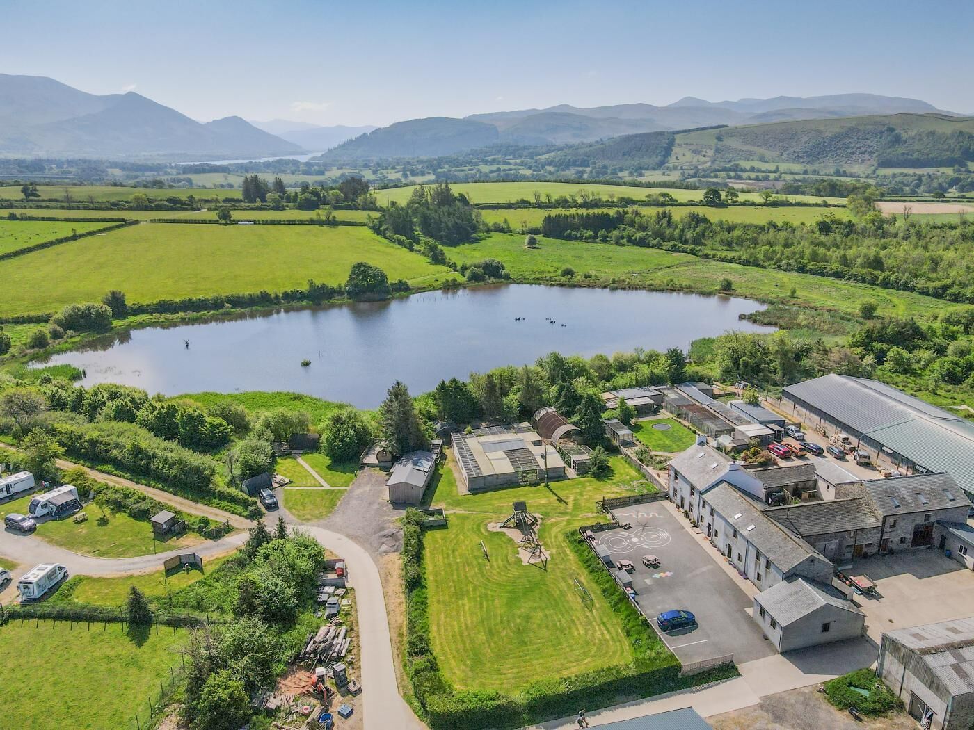 An aerial view of a rural property with a large pond, green fields, and a building complex with multiple structures.