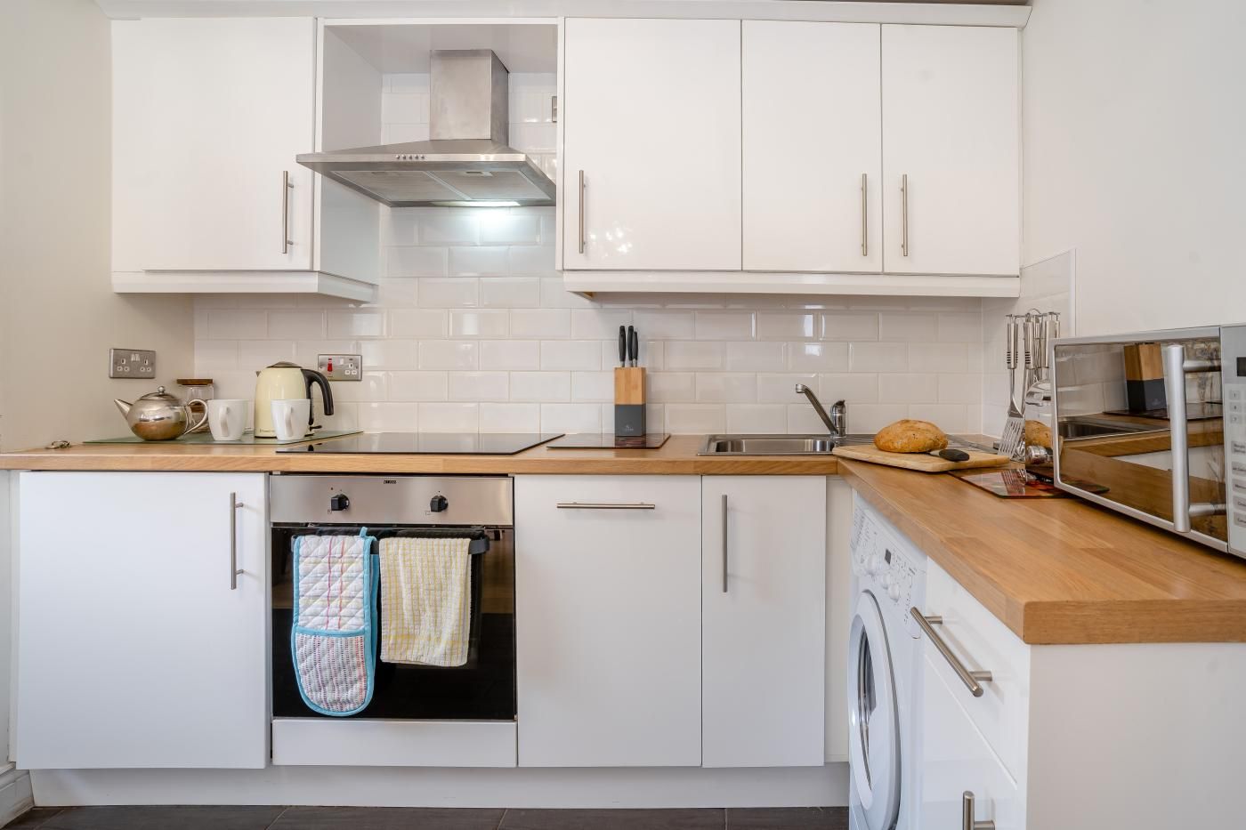 A modern kitchen with white cabinetry, stainless steel appliances, and a wooden countertop.