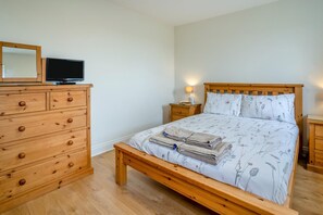Une chambre à coucher avec un lit en bois, une commode dotée de nombreux tiroirs, une table de chevet avec une lampe et un téléviseur posé sur le dessus de la commode.