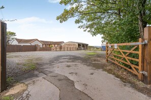 Une propriété rurale avec une allée de gravier menant à un portail en bois, des bâtiments agricoles et une zone clôturée.