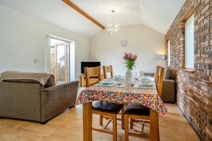 A dining area with a table set for four, a sofa, and a brick wall. - 2 Bed in Gower (oc-hh487) (Pen-clawdd)