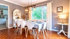 A dining area with a table set for four, white chairs, a chandelier, and a window with curtains. - 4 Bed in Swansea (oc-hh642) (Mayals)