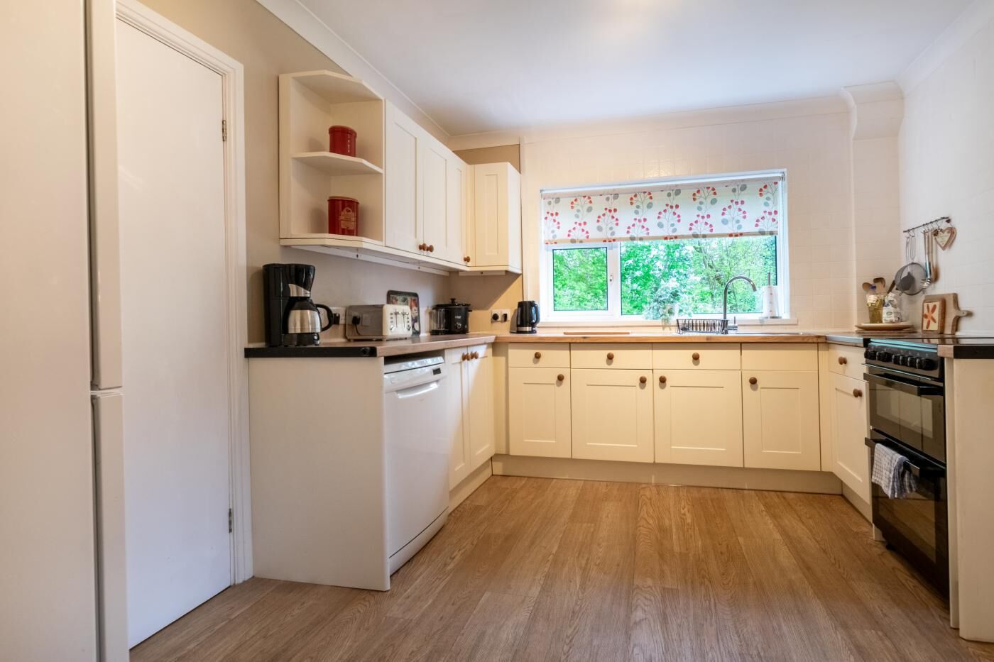 A compact kitchen with white cabinets, a built-in oven, a coffee maker, and a window with a view of greenery.