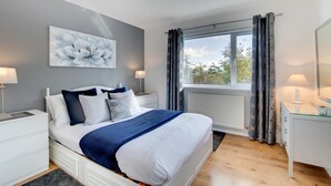 A bedroom with a bed, bedside tables, a dresser, a window with curtains, and a painting on the wall. - 4 Bed in Swansea (oc-hh642) (Mayals)