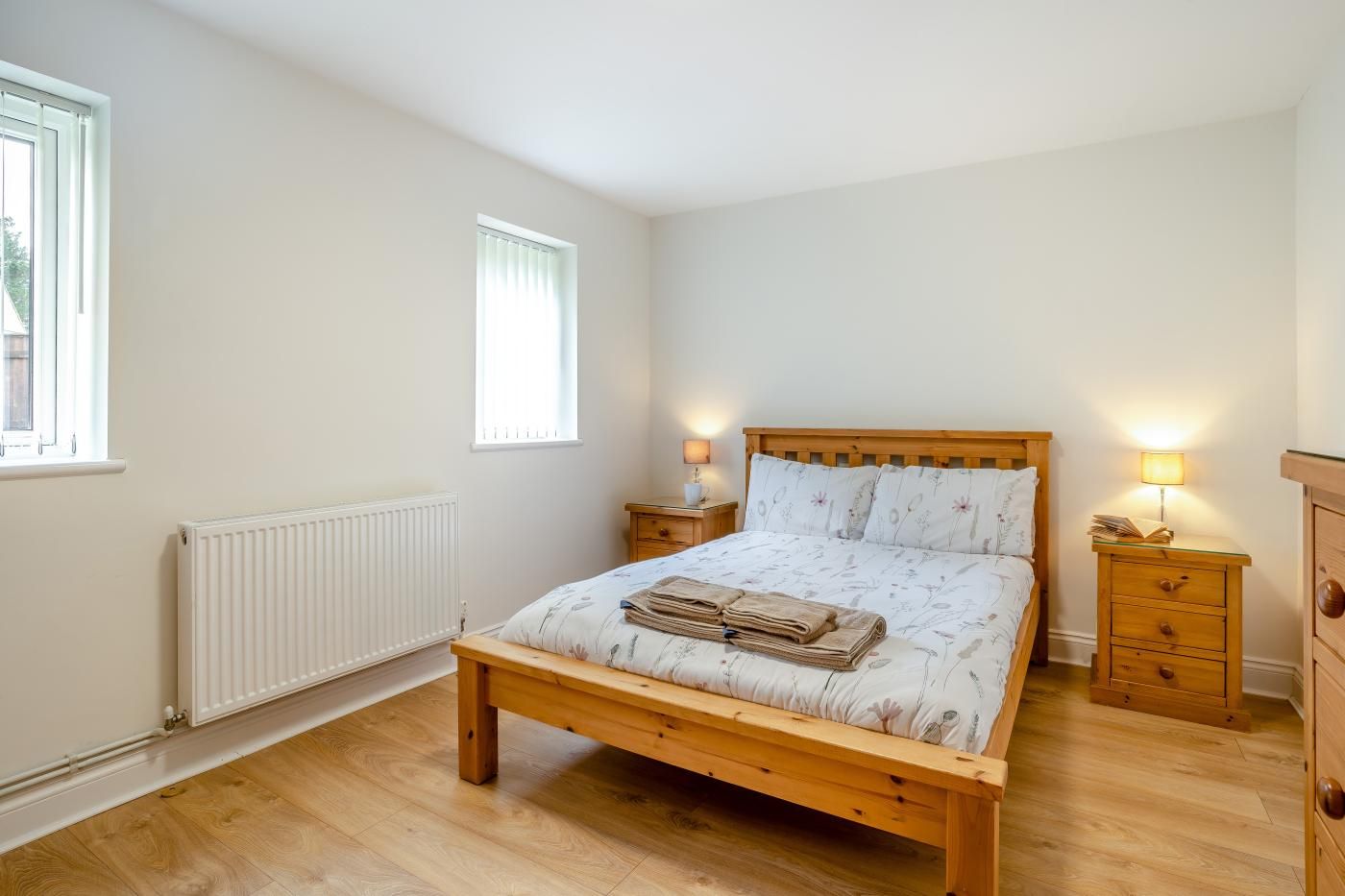 Un dormitorio con una cama de madera, dos mesitas de noche con lámparas, un radiador y una ventana.