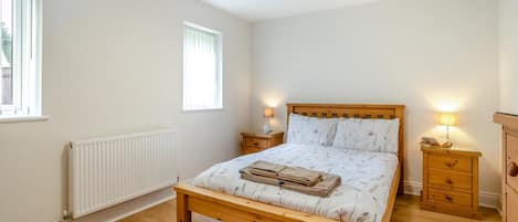 Un dormitorio con una cama de madera, dos mesitas de noche con lámparas, un radiador y una ventana.
