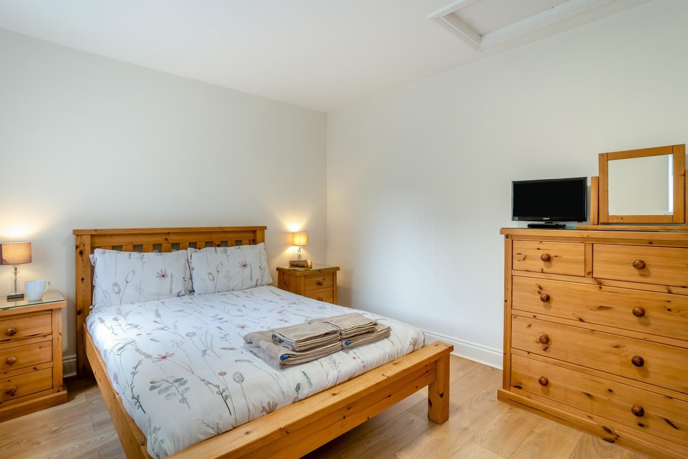 Un dormitorio con una cama de madera, mesitas de noche, un aparador y un televisor sobre un mueble.