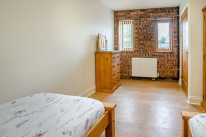 Een slaapkamer met een houten dressoir, een bed met bloemenbedekking, een bakstenen muur en een raam met jaloezieën.