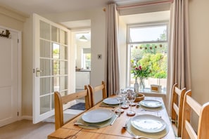 A dining area with a table set for four, a window with curtains, and a view of greenery outside.