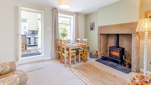 Ein gemütliches Wohnzimmer mit Kamin, einem Esstisch mit Stühlen und einer durchgehenden Tür erkennbaren Küche.