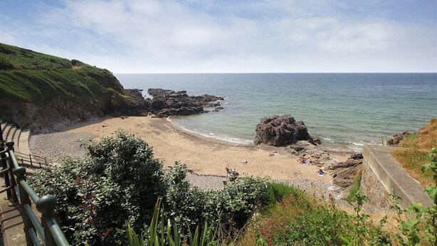 Eine Küstenlandschaft mit Sandstrand, Felsformationen und blauem Himmel.