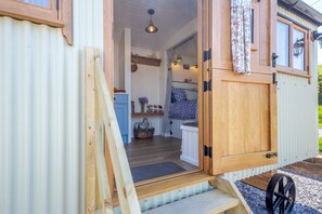 A wooden door leading to a room with a bed, a small table, and a shelf with items. - 1 Bed in Llannefydd (oc-p32089) (Llannefydd)