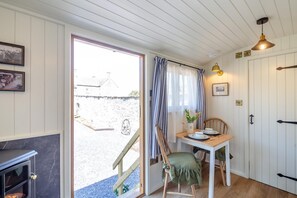 A room with a wooden dining table, chairs, a small kitchen area, and a view of the outside. - 1 Bed in Llannefydd (oc-p32089) (Llannefydd)