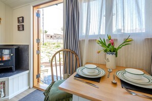 A dining area with a table set for two, a vase with flowers, and a view through a door to the outside. - 1 Bed in Llannefydd (oc-p32089) (Llannefydd)