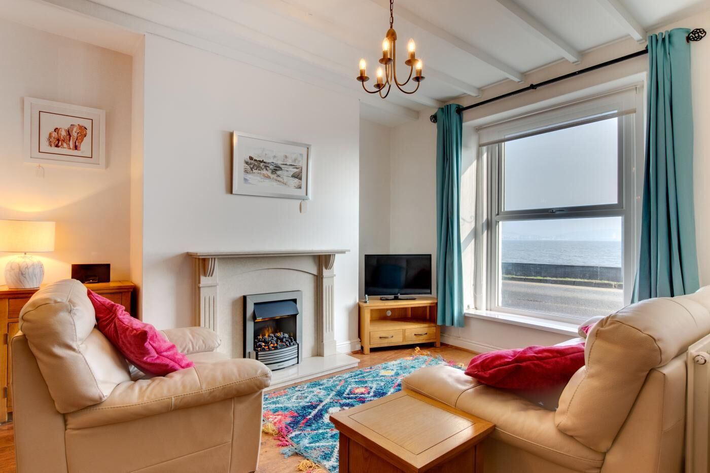A living room with a fireplace, television, and a view of the sea.