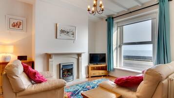 A living room with a fireplace, television, and a view of the sea.