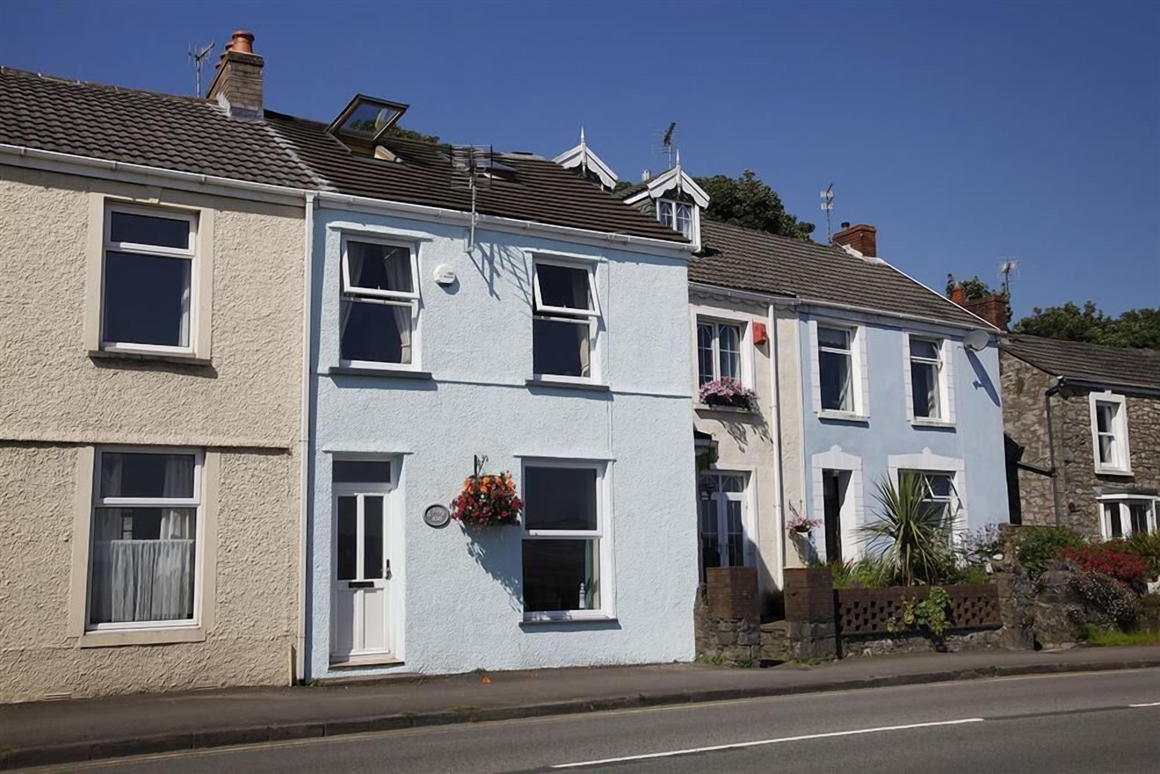 A row of two-story houses with white and light blue exteriors, multiple windows, and small balconies with flower boxes.