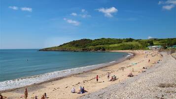 A beach with people sunbathing and swimming, a rocky shoreline, and a hill with greenery in the background.