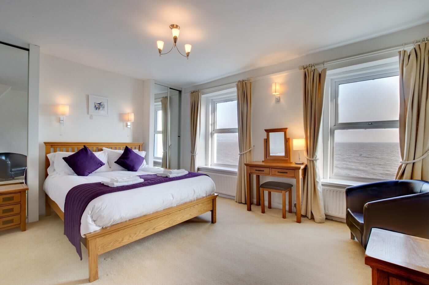 Une chambre d’hôtel avec un lit, un bureau, une chaise, un miroir et une vue sur la mer.