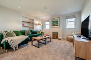 Ein modernes Wohnzimmer mit einem grünen Sofa, einem Holztisch, einem Kamin und einem Fernseher.