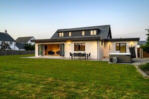 Ein modernes, zweistöckiges Haus mit Terrasse, Sitzgelegenheiten im Freien und einem Whirlpool.