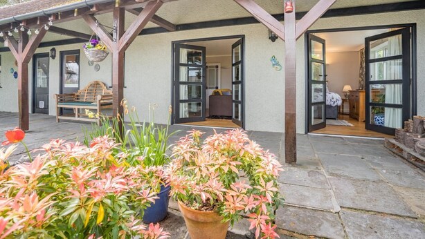 Ein überdachter Außenbereich mit einer Bank, Topfpflanzen und einer Holz-Pergola.