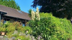 Ein Haus mit geneigtem Dach, umgeben von einem gepflegten Garten mit verschiedenen Pflanzen und Blumen.