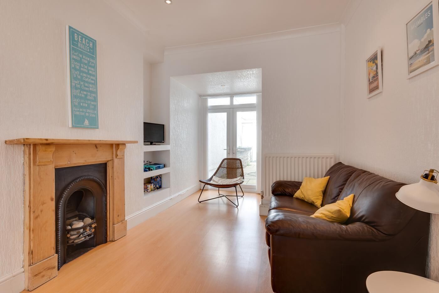 Una sala de estar con chimenea, un sofá de cuero marrón con cojines amarillos, un televisor en un estante y una ventana con vistas.