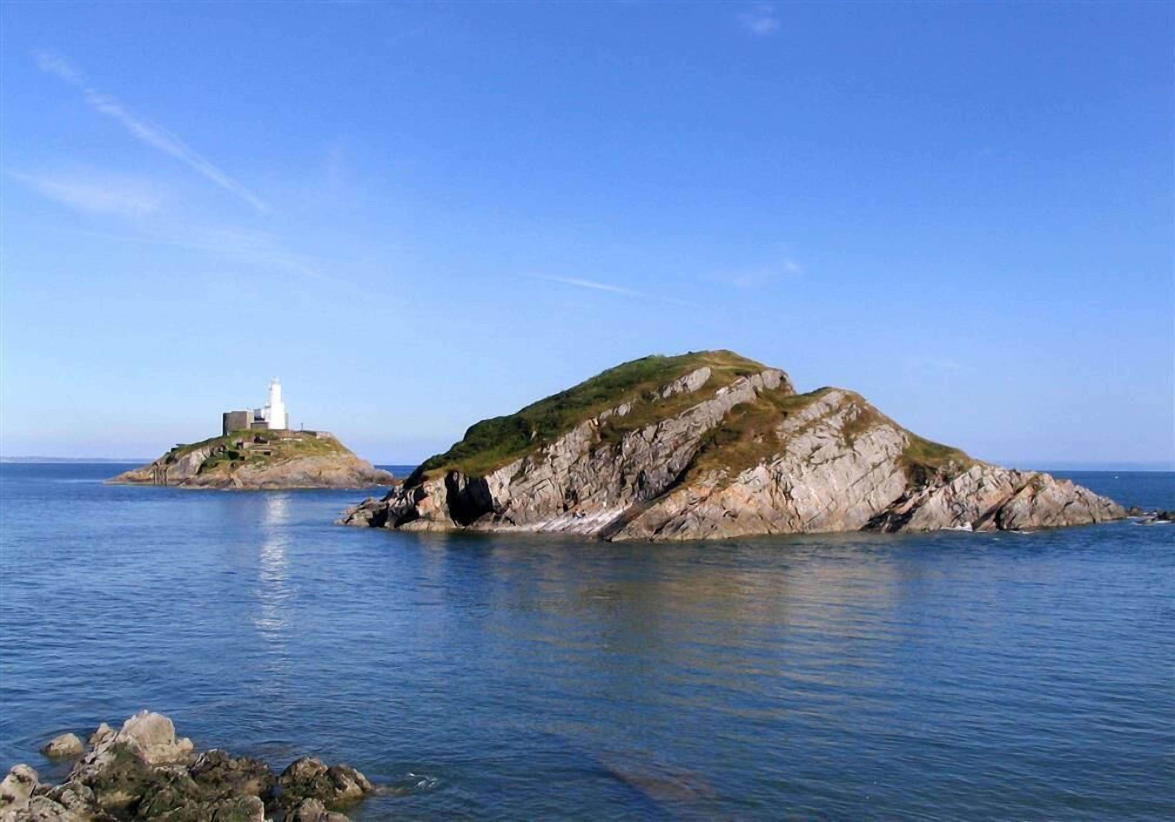 Ein Leuchtturm auf einer kleinen Insel mit felsigem Gelände und ruhigem Wasser.