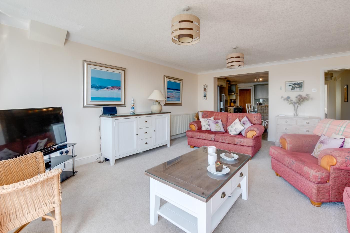 A living room with a TV, white cabinet, pink sofa, wicker chair, and a glass coffee table.