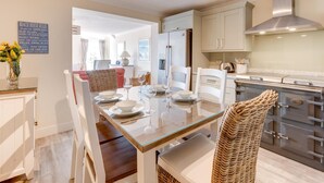 Une cuisine moderne avec des armoires blanches, une hotte en acier inoxydable et un coin repas comprenant une table en verre et des chaises blanches.