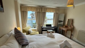 Une chambre d’hôtel avec un lit, un piano, un bureau et une vue sur la mer.