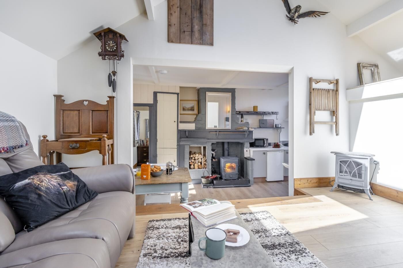 A cozy living room with a sofa, a coffee table, and a fireplace. There is a kitchen area with a stove and a microwave visible.