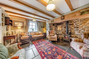 Ein gemütliches Wohnzimmer mit Kamin aus Stein, Holzbalken und einem großen Teppich.