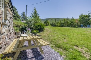 A stone building with a wooden table set for dining, surrounded by a grassy area and trees. - 4 Bed in Arthog (oc-b31966) (Arthog)