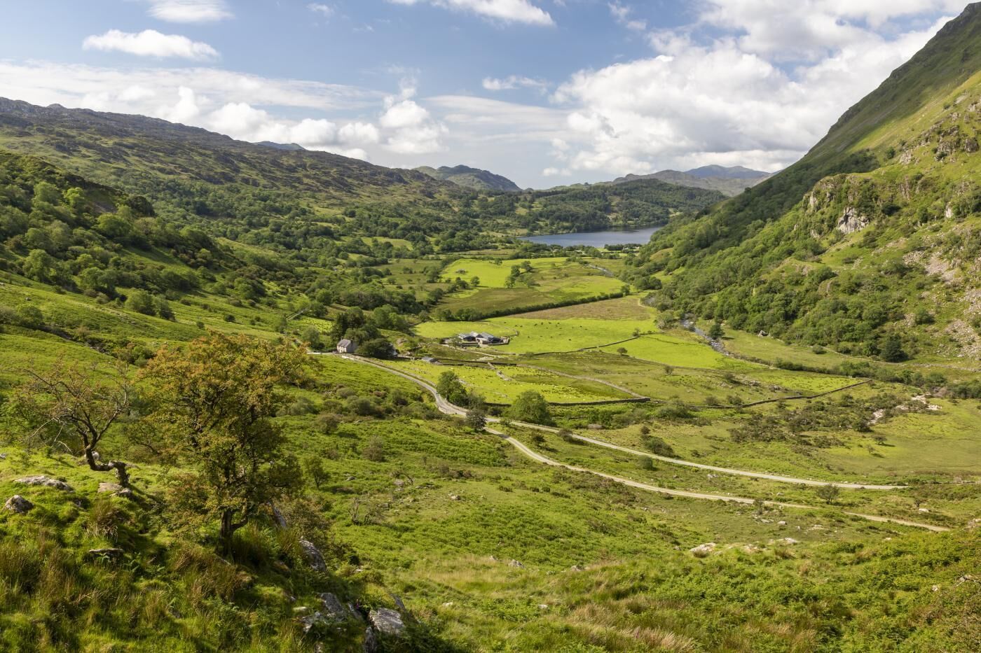A valley with a lake, surrounded by green hills and a few buildings.