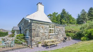 A stone house with a chimney, a wooden bench, and a picnic table.