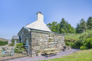 Una casa de piedra con chimenea, un banco de madera y una mesa de picnic.